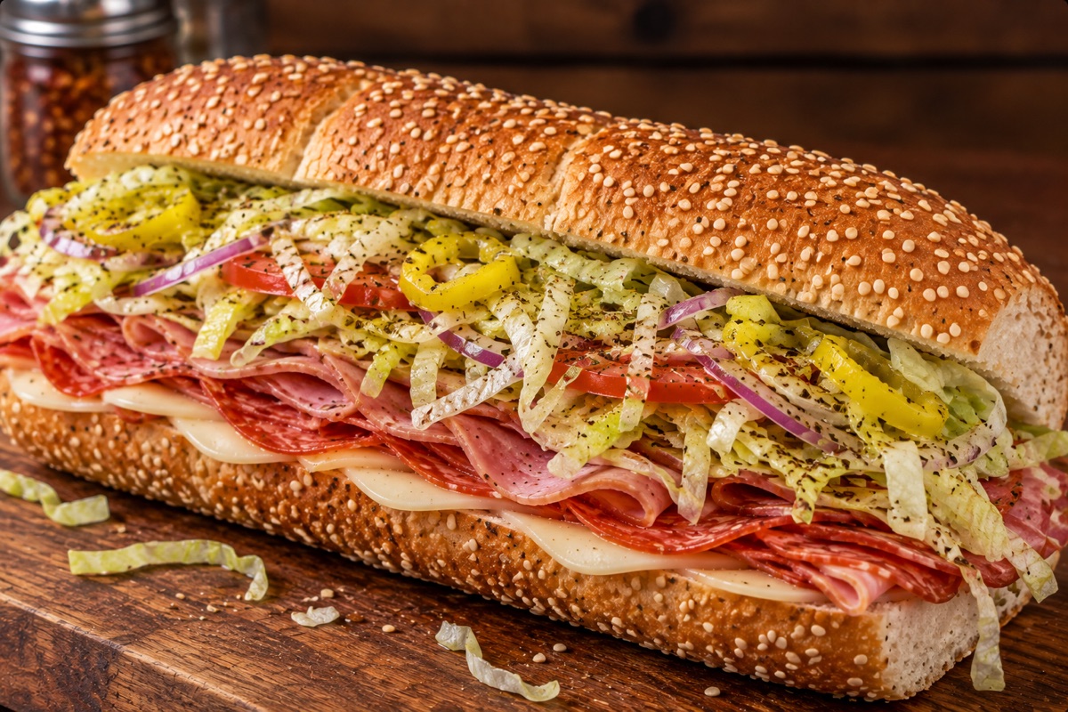 An Italian grinder stacked with salami, ham, provolone, lettuce, tomato, onion and hot peppers